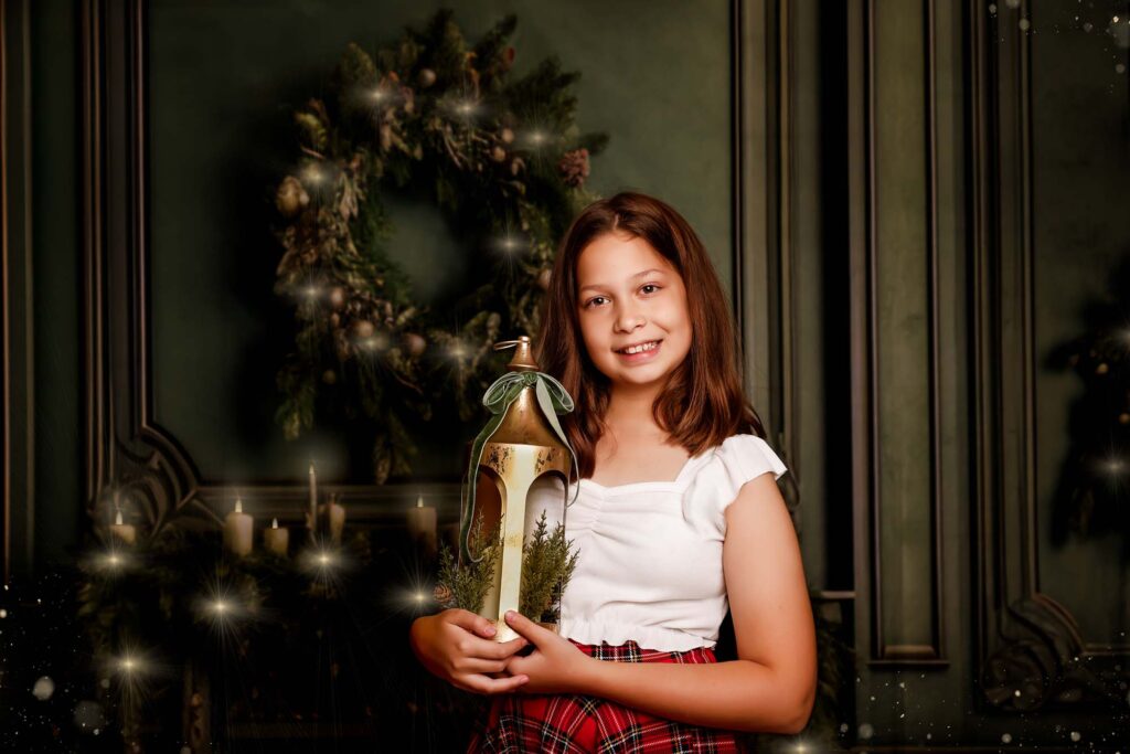 Girl holding a festive lantern in front of the Christmas wreath and fireplace